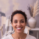 Portrait of a diverse woman in her late 20s to early 30s, smiling warmly, against a backdrop of dusty lilac and warm cream.