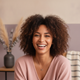Close-up portrait of a smiling woman with warm, friendly eyes, conveying trust and happiness against a soft, cream and lilac 