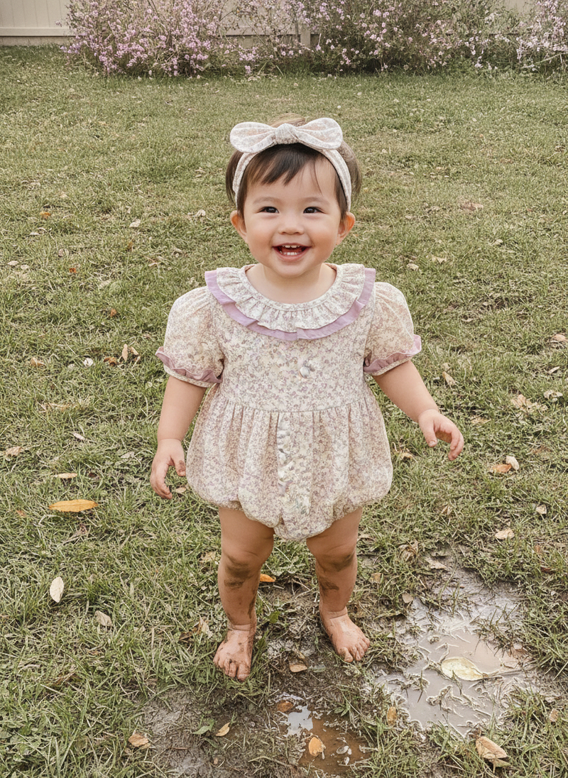 Toddler boy with diverse ethnicity wearing a sky blue romper, playing happily in a muddy backyard on a sunny day.